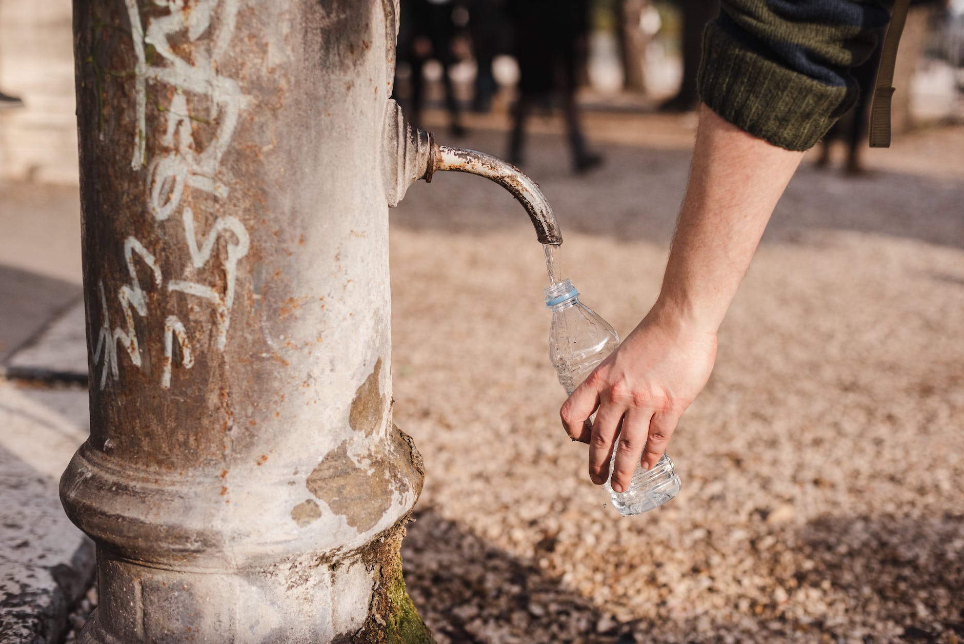 crop person filling bottle with water from drinking fountain